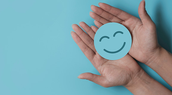 two hands holding a smiling face icon on a blue background